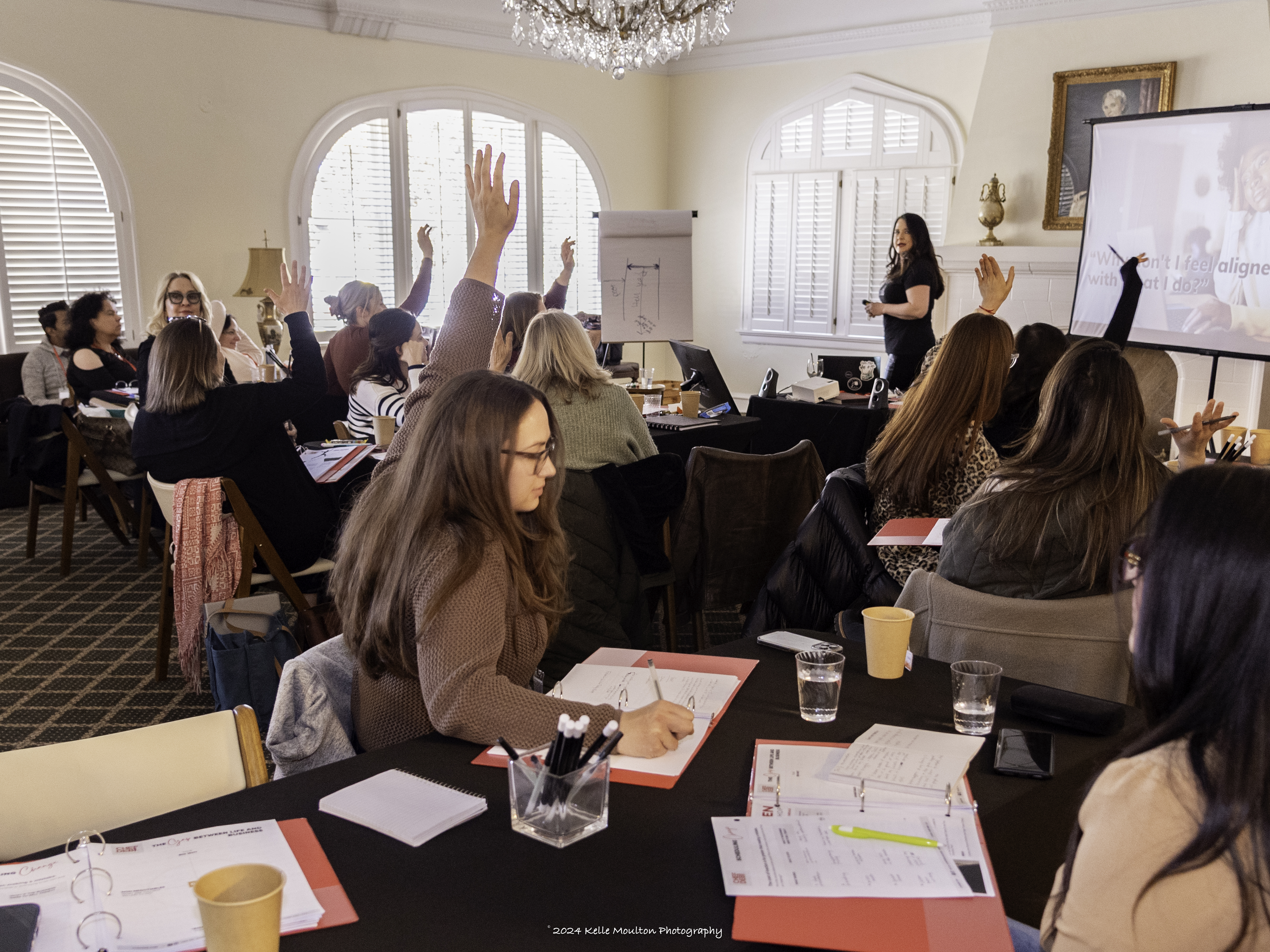 SHARPEN attendees seated at worktables with hands raised during a session